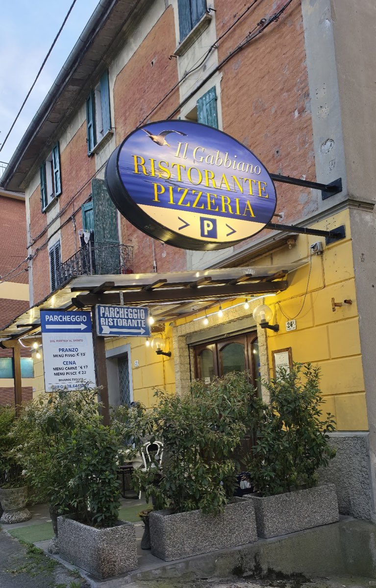 L'insegna ovale blu con il gabbiano e la facciata gialla del ristorante Il Gabbiano
